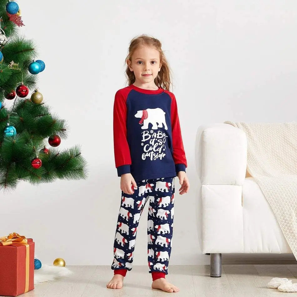 Child wearing Christmas family matching pyjamas with polar bear print near decorated tree and red gift box