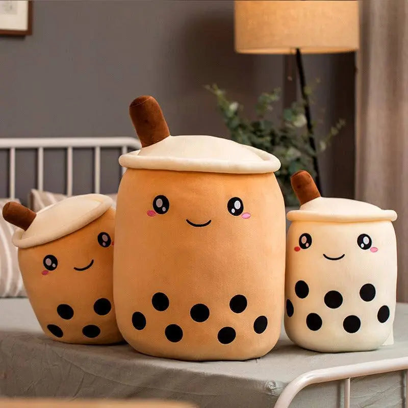 Three plush boba stuffed toys in varying sizes with cute smiling faces and black tapioca pearls on a bed