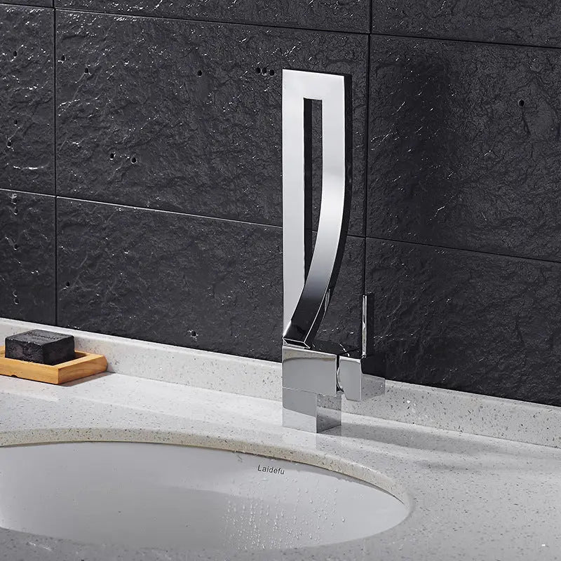 Chrome faucet on a bathroom sink with dark tiled wall in the background
