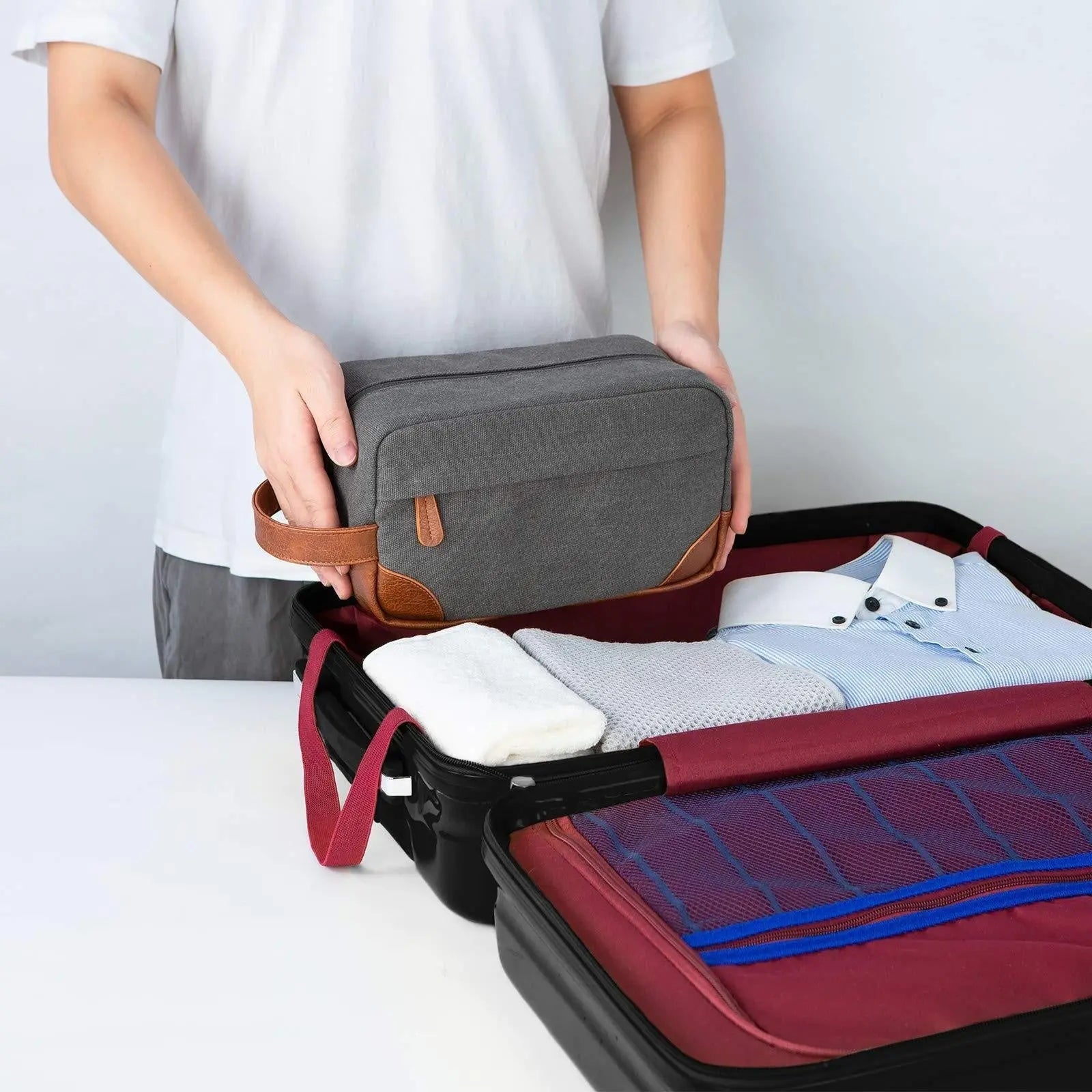 Men's toiletry large capacity travel bag in gray canvas with leather accents being packed into suitcase