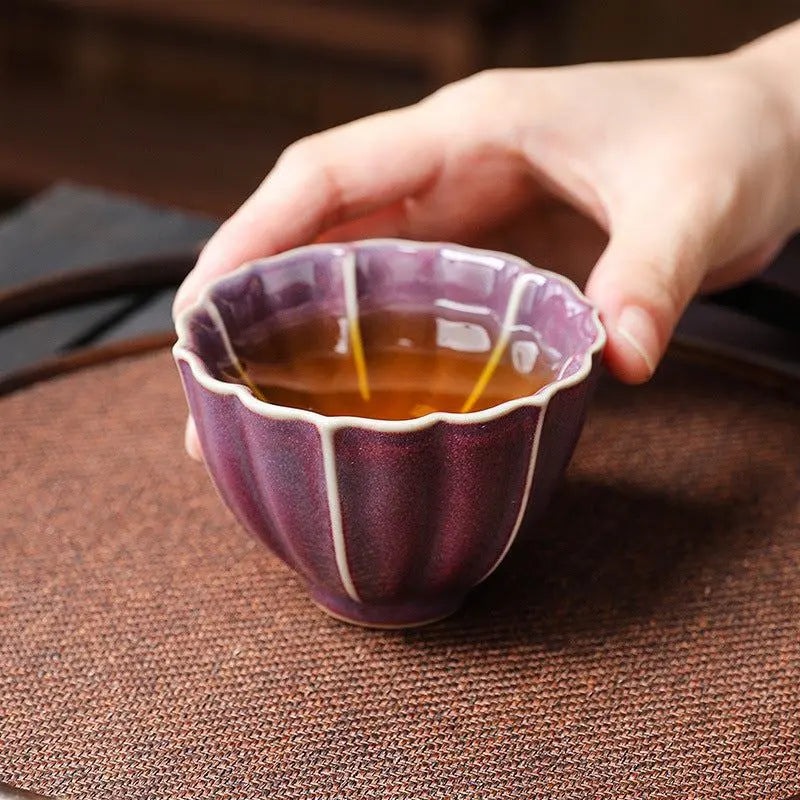 Traditional Chinese ceramic teacup with purple glaze, held in hand, for tea ceremonies and gifting