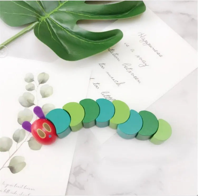 Colorful caterpillar toy on a white surface with green leaves and small plants.