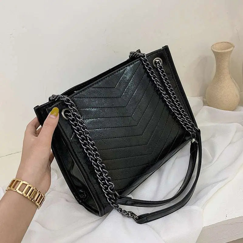 Black PU leather ladies messenger bag with chain shoulder straps and zipper closure, featuring fine car suture detailing and a chic plain design.
