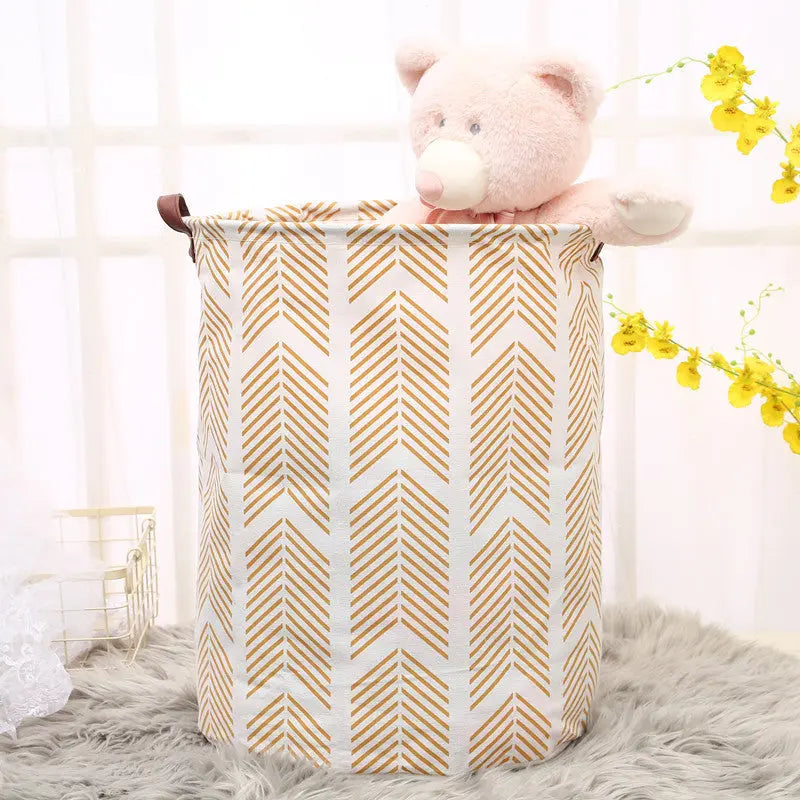 Hamper with gold chevron pattern held by a pink teddy bear on a soft surface.