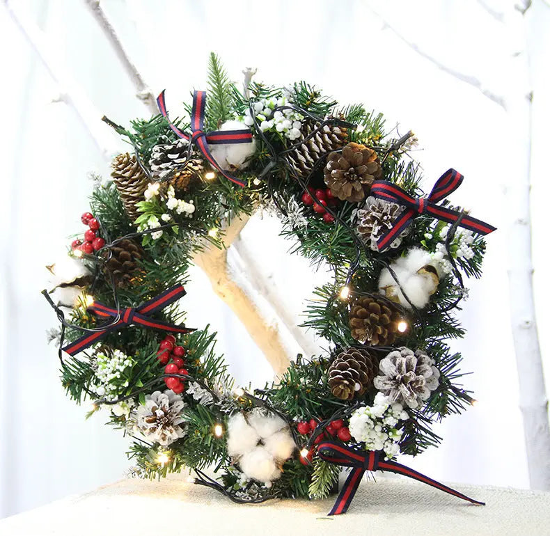 Christmas wreath hanging decoration with pinecones, red berries, cotton accents, and ribbon bows on green garland with lights