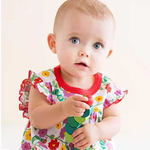 Baby wearing a colorful floral dress holding a toy