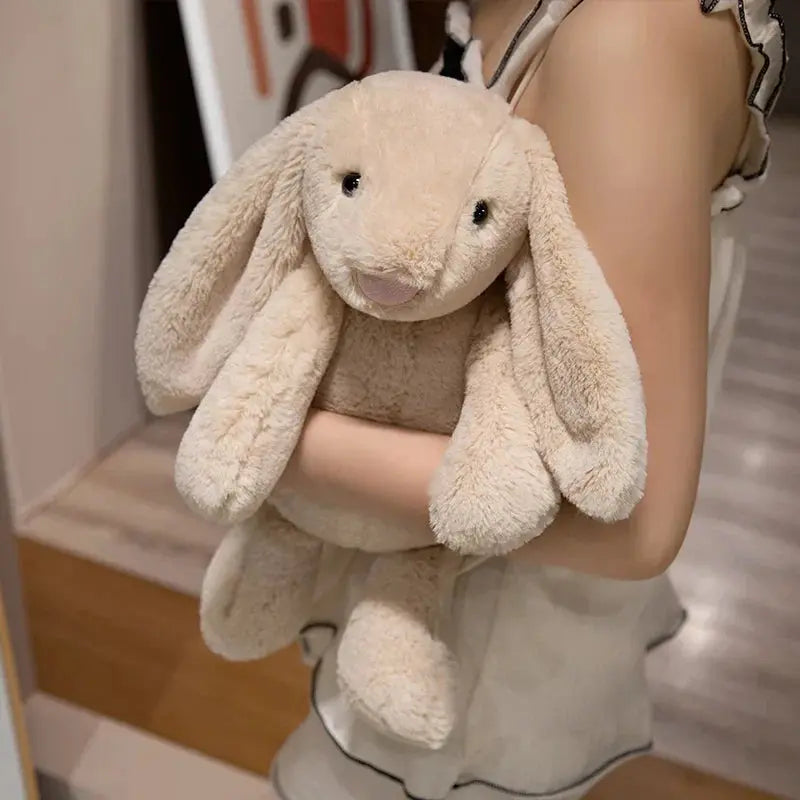 Person holding a large beige plush bunny toy indoors.
