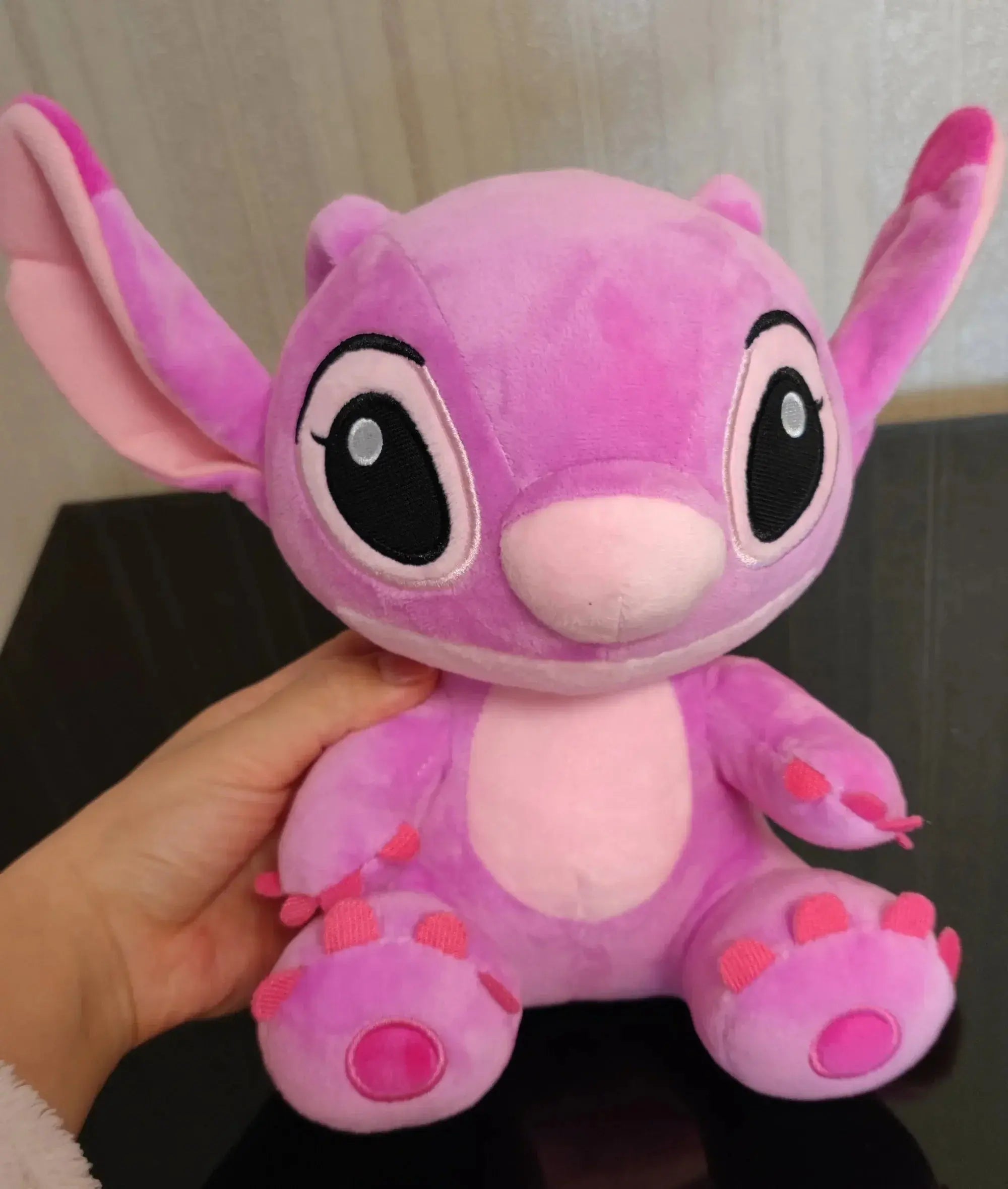 Pink plush toy with large eyes held by a hand against a neutral background