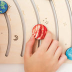 Hand placing a red planet model on a wooden solar system model