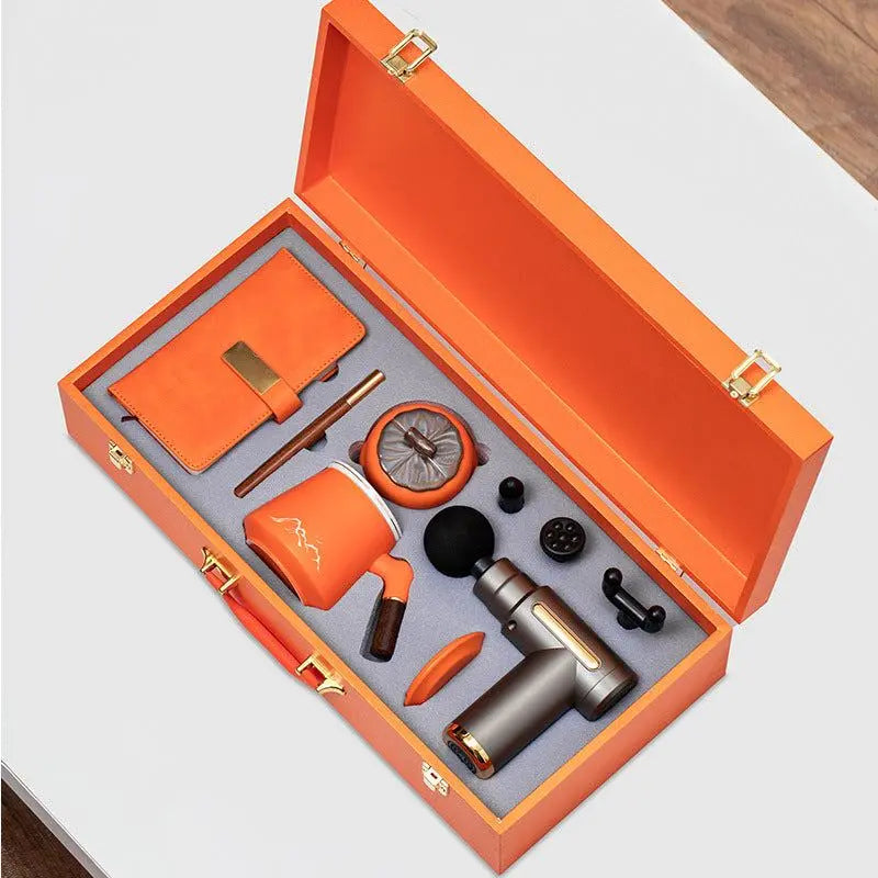Orange massage gun gift box set with notebook, pen, mug, and multiple massage heads in premium packaging