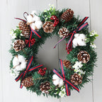 Christmas wreath hanging decoration with pinecones, cotton, red berries, and ribbon on green PVC garland