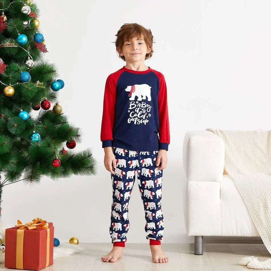Child wearing Christmas Family Matching Pyjamas with polar bear print by decorated Christmas tree and gift box
