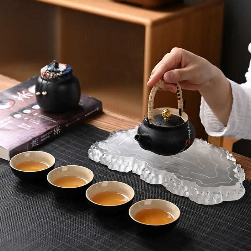 Ceramic Kung Fu tea set with black teapot and four cups on a textured mat, pouring tea in a modern traditional style.